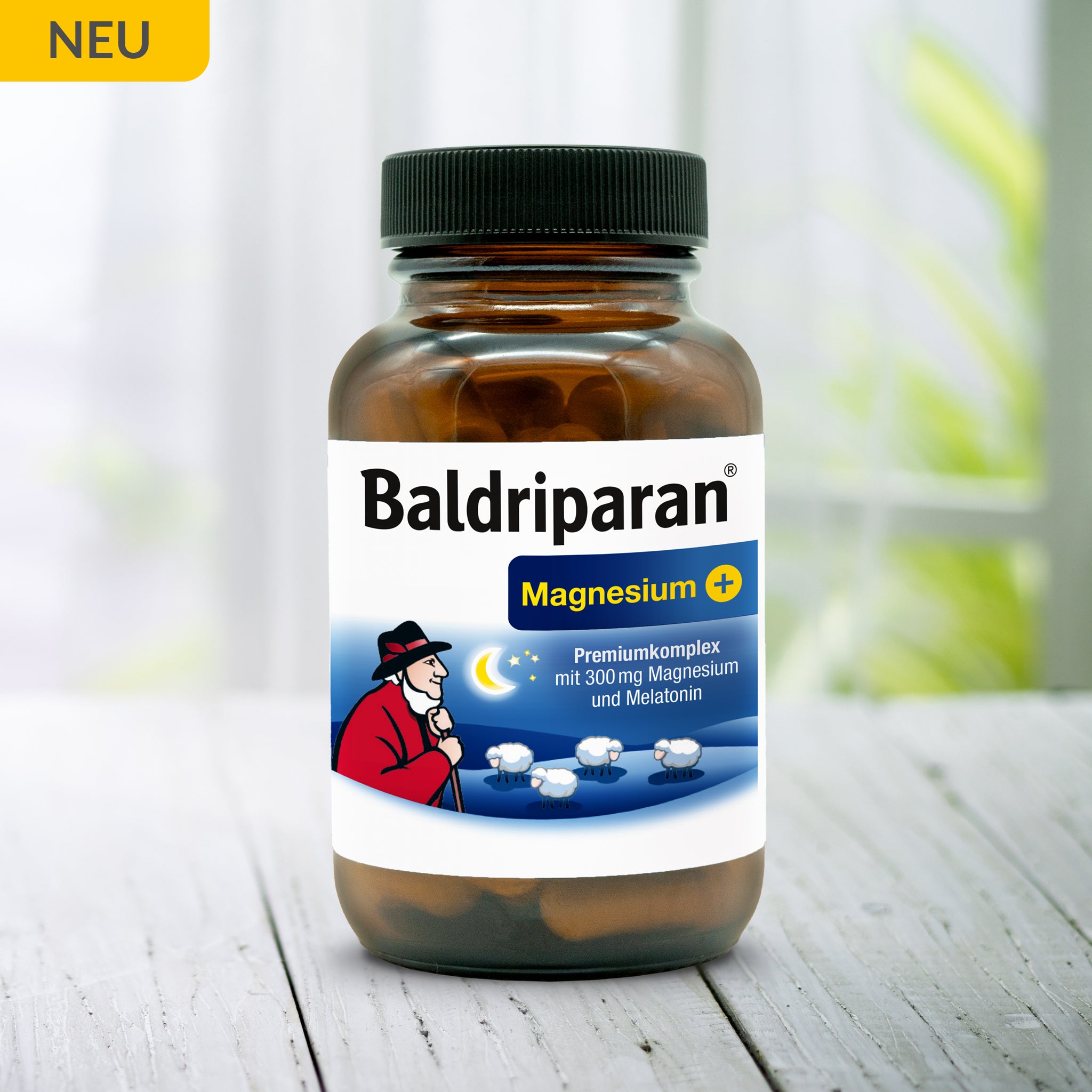 Flasche Baldriparan® Magnesium+ mit 300 mg Magnesium und Melatonin auf hellem Holztisch. Hinweis: „Neu“. Etikett zeigt Hirtenfigur, Nachtmotiv und Schäfchen.
